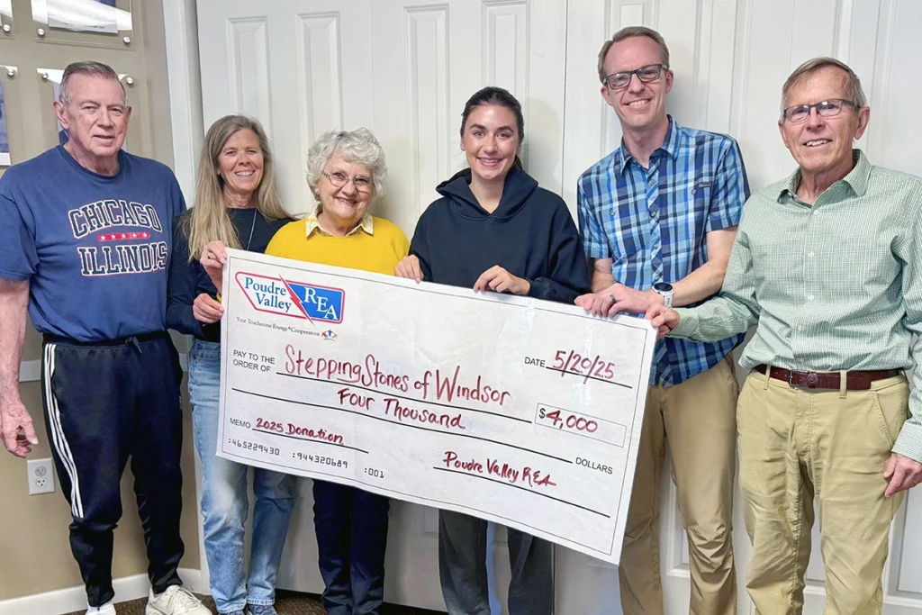 Six people stand indoors, holding an oversized check for $4,000 made out to Stepping Stones of Windsor from Poudre Valley REA, dated 5/20/25.