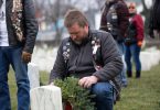 man placing Christmas wreath on grave