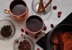 Two mugs of spice mulled wine mocktail surrounded by ingredients