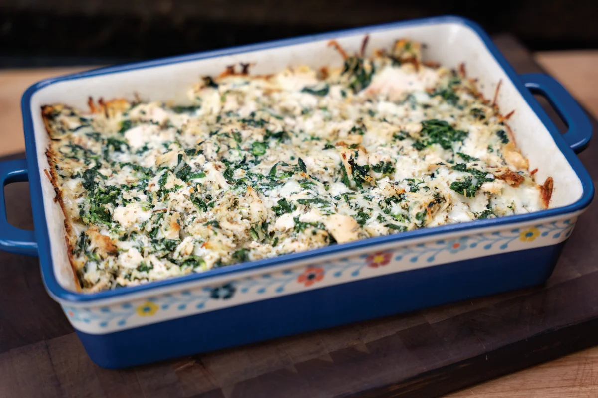 A blue casserole dish filled with a baked spinach and cheese casserole, resting on a wooden surface.