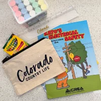 A collection of items including a box of chalk, a Crayola crayon box, a Kato’s Electrical Safety coloring book, and a Colorado Country Life pouch on a speckled surface.
