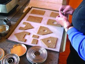 Person preparing gingerbread house pieces on a baking tray with various circular cookie cutters nearby.