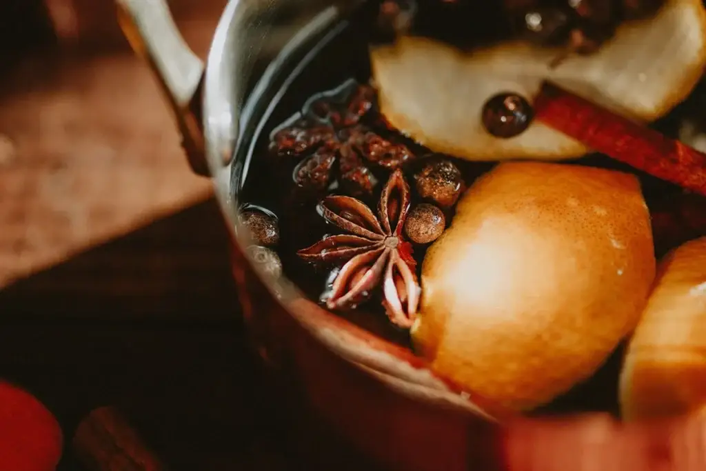 A close-up of a pot containing lemon slices, star anise, cinnamon sticks, and other whole spices in a dark liquid.