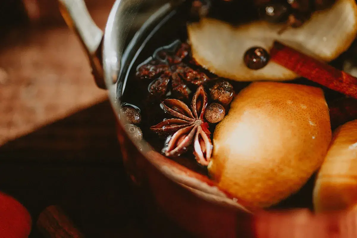A close-up of a pot containing lemon slices, star anise, cinnamon sticks, and other whole spices in a dark liquid.