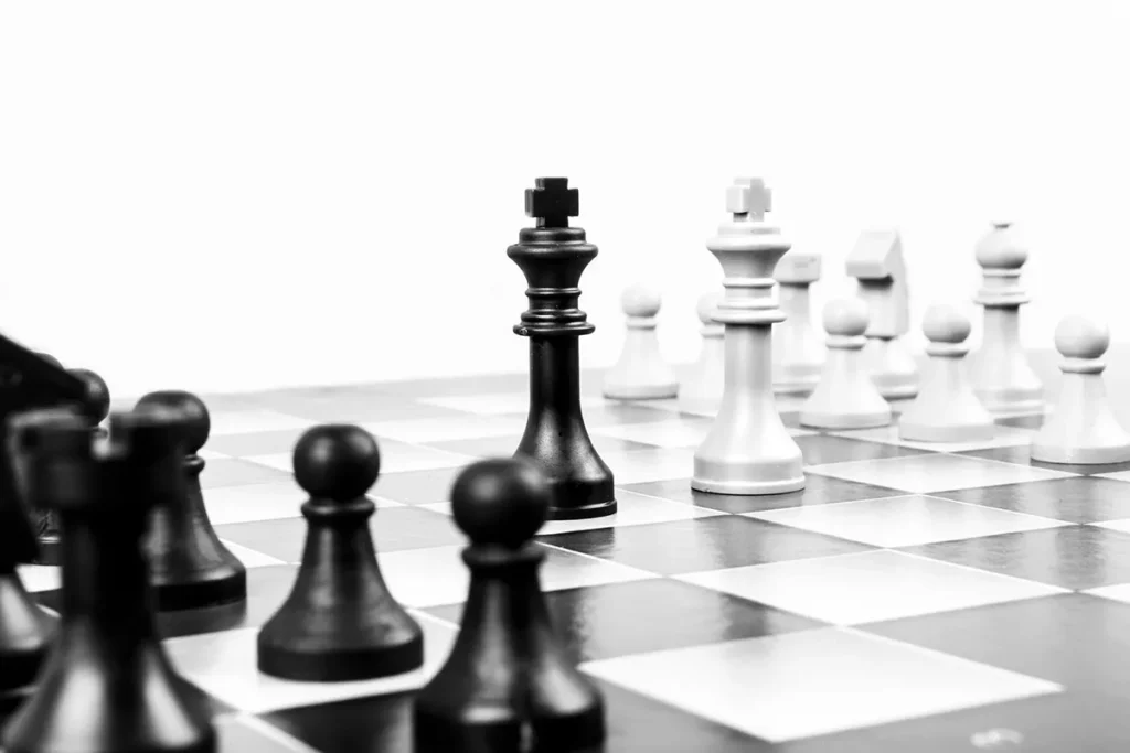 A black king and a white king face each other on a chessboard surrounded by various chess pieces, with a white background.