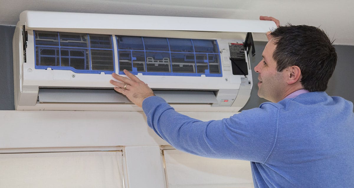 A person in a blue sweater adjusts or installs a wall-mounted air conditioning unit indoors.
