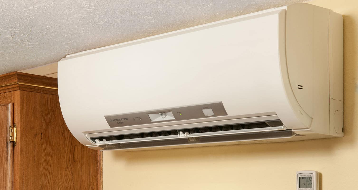Wall-mounted white air conditioning unit with control panel, situated next to a wooden cabinet.
