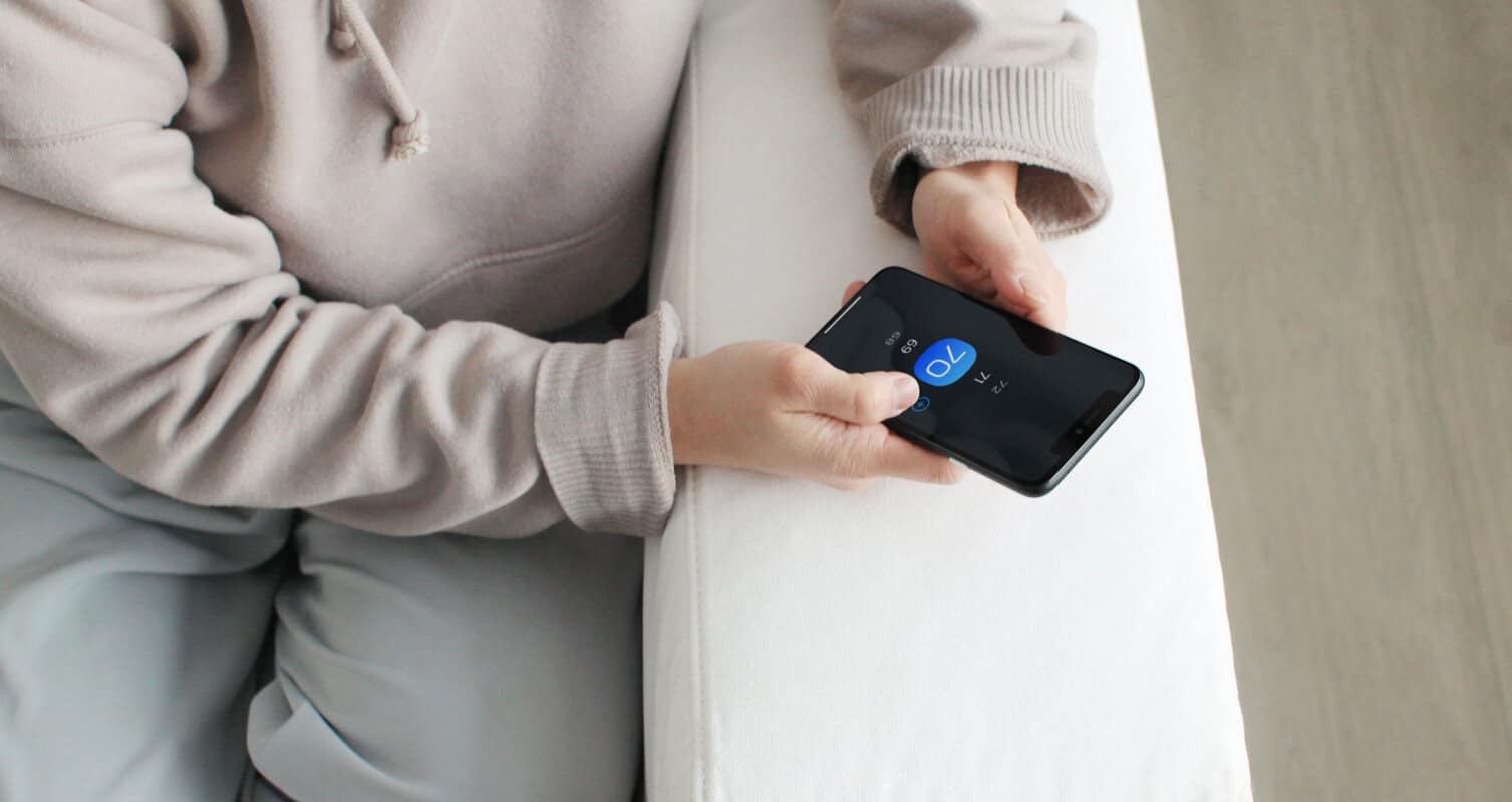 Person sitting on a couch, holding a smartphone displaying a timer set at 10 seconds.