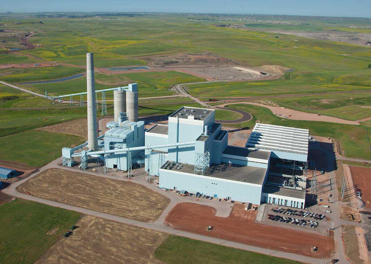 Aerial view of a large industrial power plant with tall smokestacks, surrounded by vast green fields and roads.