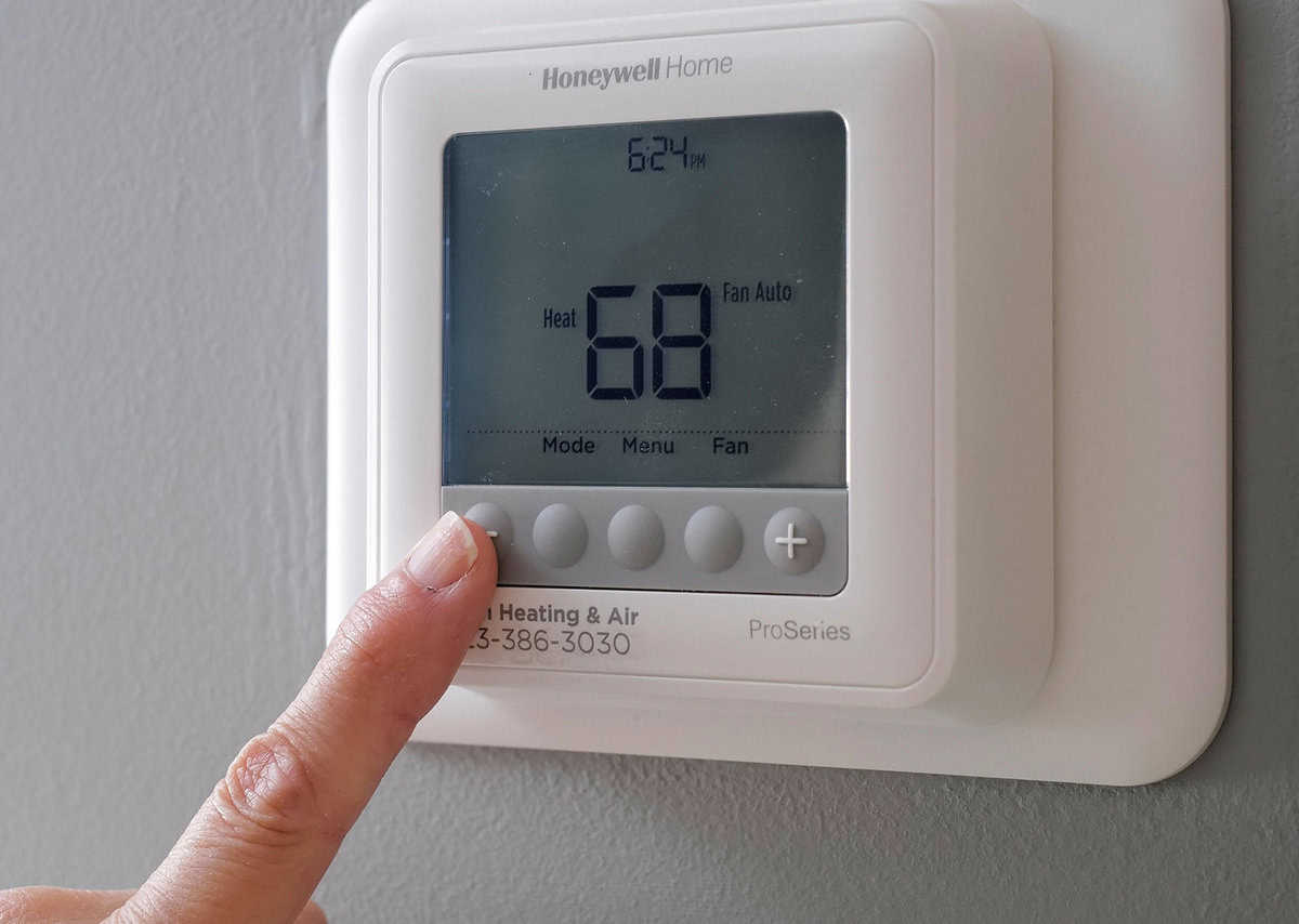 A hand adjusts the temperature on a Honeywell Home ProSeries thermostat set to 68 degrees.