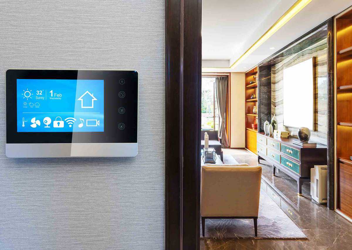 Smart home control panel on a wall displays weather, date, and security icons; modern living room visible in the background.