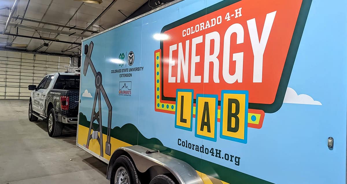 Trailer with "Colorado 4-H Energy Lab" branding parked in a garage next to a vehicle.