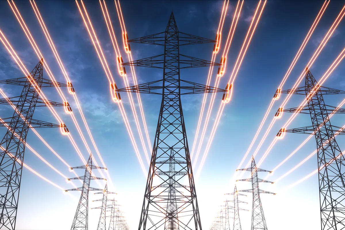 Multiple electrical transmission towers with glowing power lines stretch into the distance against a blue sky.