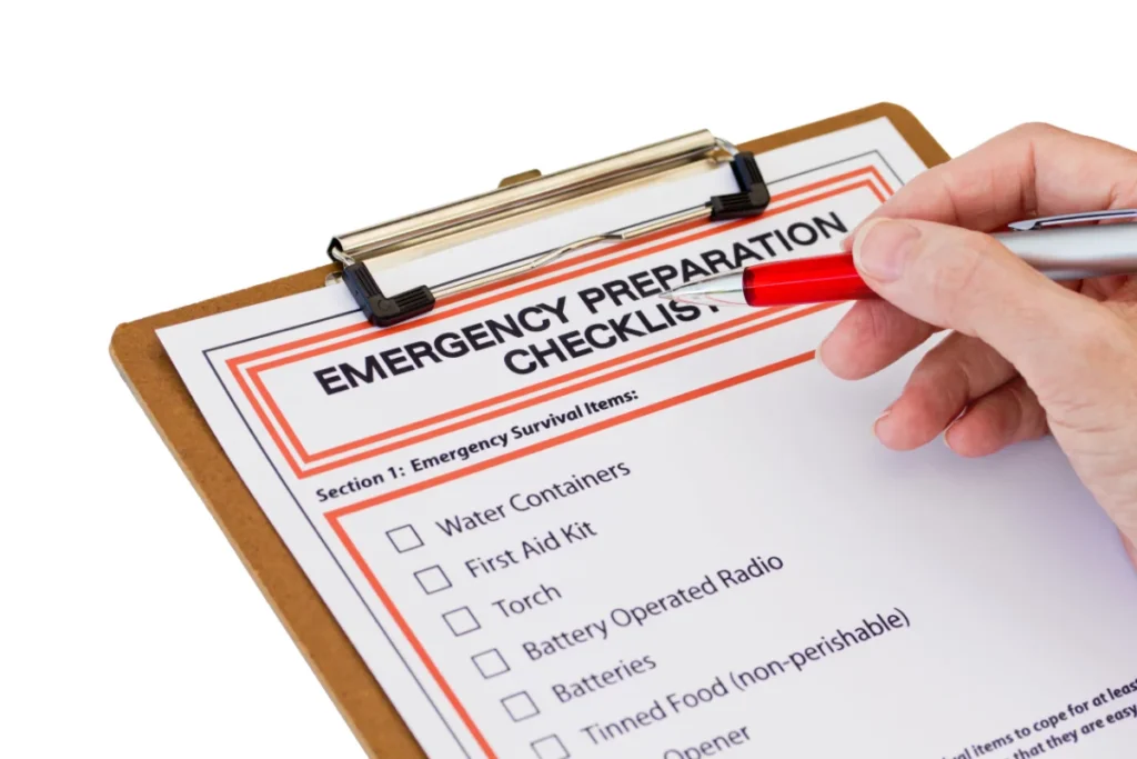 A hand holding a pen hovers over a clipboard with an "Emergency Preparation Checklist" that includes items like water containers, first aid kit, torch, radio, batteries, and tinned food.