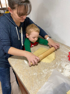 Adult and child rolling out dough on a kitchen counter, with flour and a baking tray nearby.