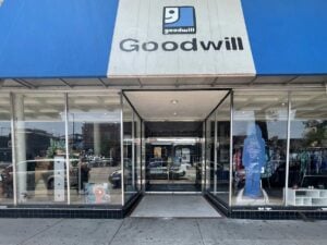 Exterior view of a Goodwill store with large glass windows displaying various items. Blue and white signage above the entrance.