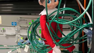 A toy elf is tangled in green cables in front of a server rack.