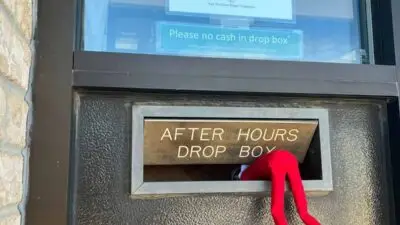 Red toy legs stick out of an after-hours drop box on a door beneath a sign indicating office hours and contact information.