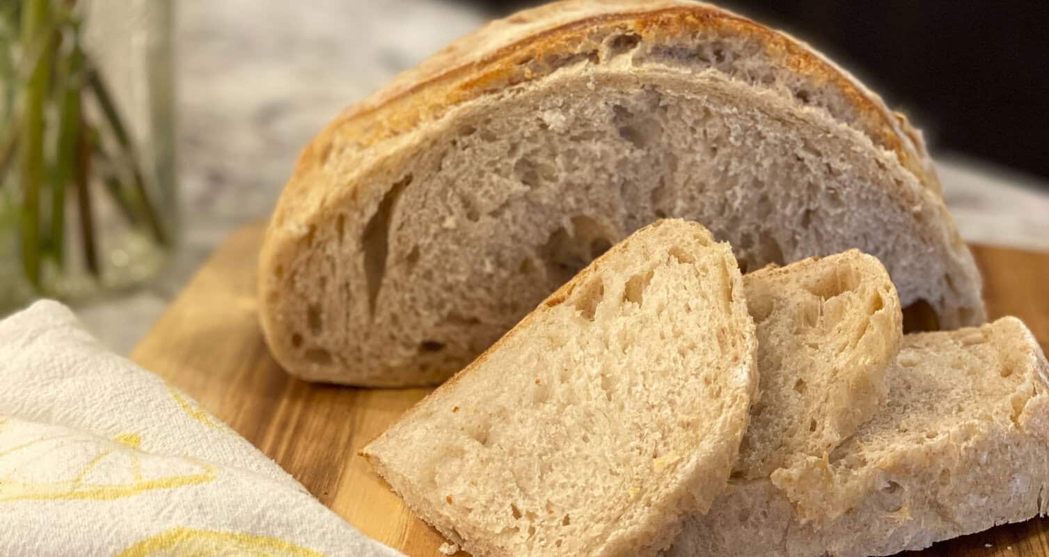 Sliced loaf of rustic bread on a wooden board, with a white cloth napkin nearby.
