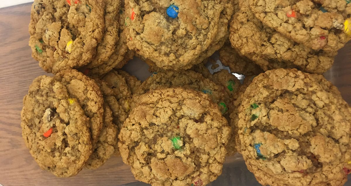 A batch of oatmeal cookies with colorful candy pieces on a wooden surface.