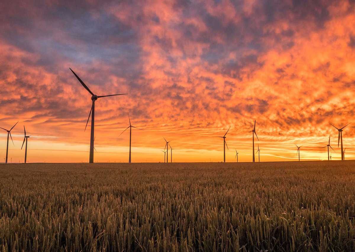 Wind turbines in a field at sunset with an orange and pink sky.