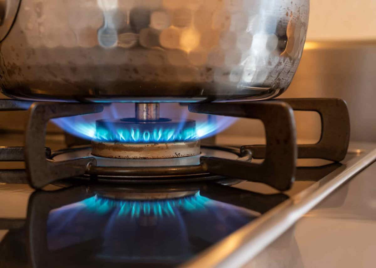 A stainless steel pot sits on a gas stove burner with a blue flame.