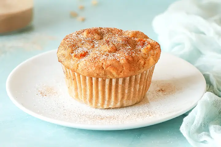 A single muffin topped with cinnamon sugar sits on a white plate against a light blue background.