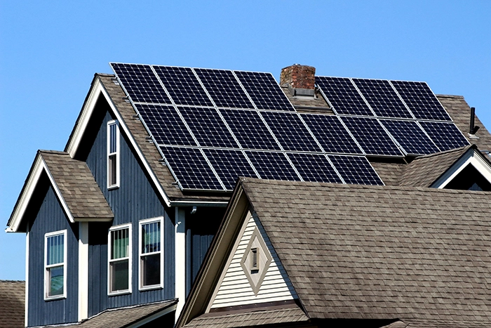 A house with multiple solar panels installed on its roof, under a clear blue sky.