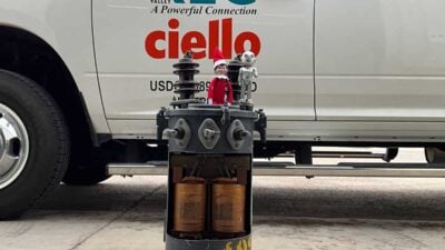 Small elf doll and a mouse figurine placed on a large electrical component in front of a parked vehicle with company logos.