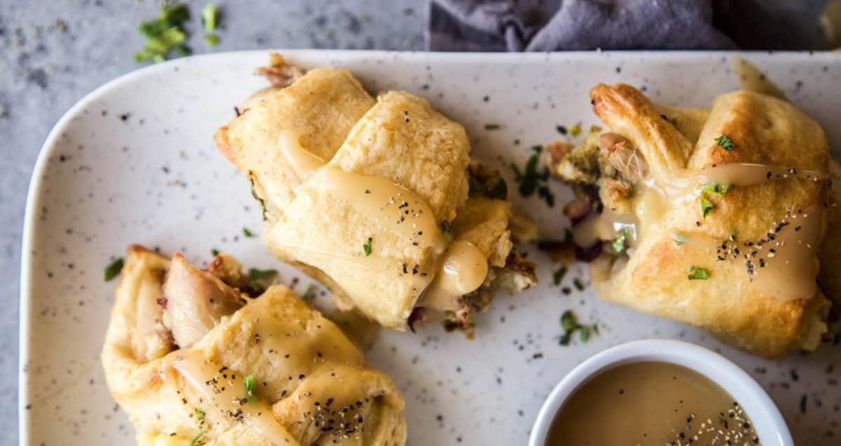 Three stuffed pastry rolls topped with sauce are on a speckled plate, accompanied by a small bowl of dipping sauce.