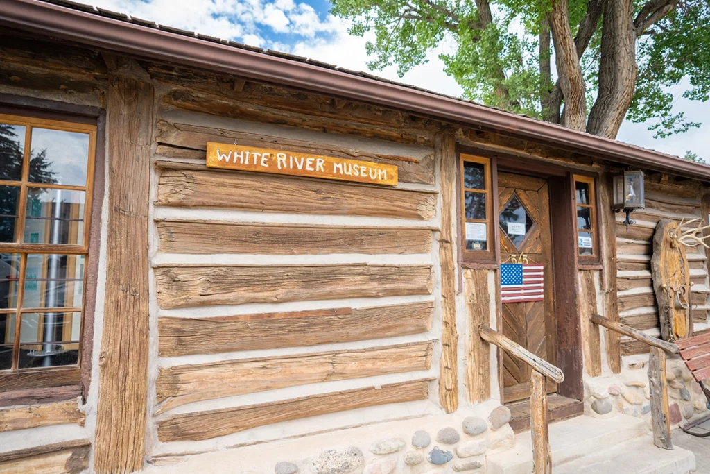 Exterior of the White River Museum, a rustic log building with a wooden sign, windows, and an American flag near the entrance.